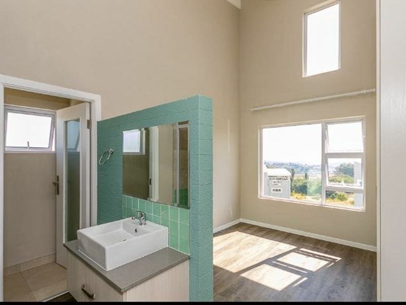Spacious bedroom featuring double volume ceilings, laminate flooring, and an integrated vanity area with a modern basin and tiled splashback.