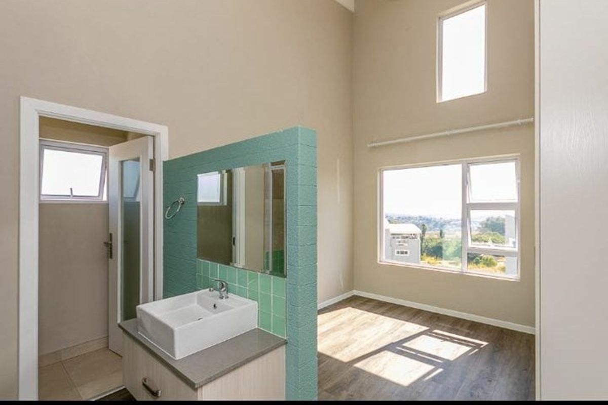 Spacious bedroom featuring double volume ceilings, laminate flooring, and an integrated vanity area with a modern basin and tiled splashback.