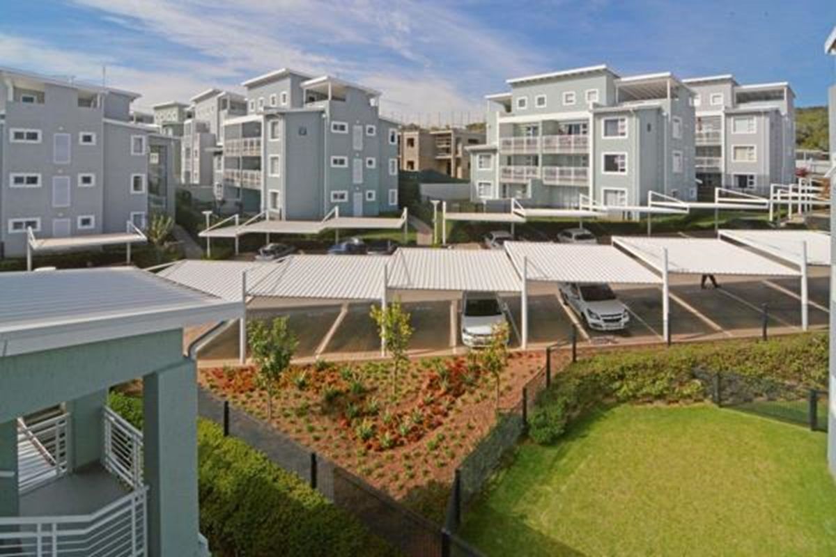 An elevated view of an apartment complex featuring multiple residential buildings, covered parking bays, and well-maintained landscaped garden areas.