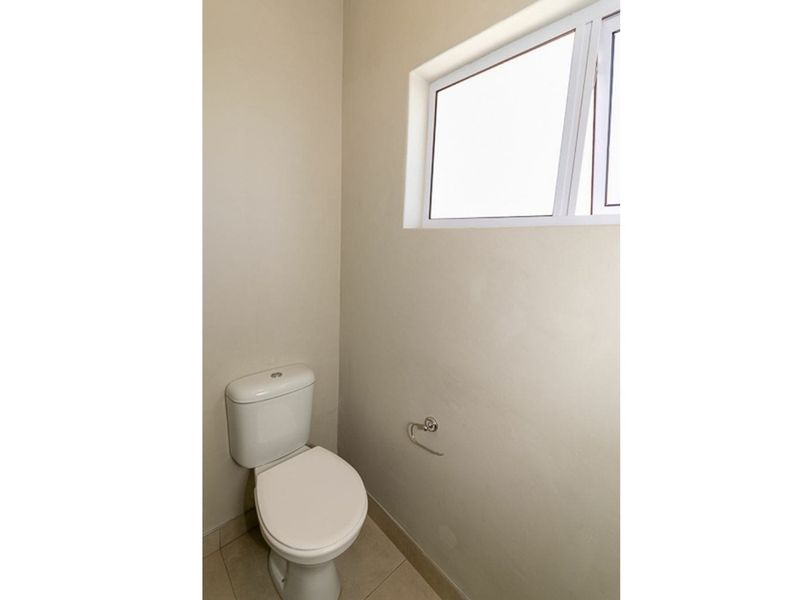A compact, functional bathroom featuring a standard toilet, tiled flooring, and a small casement window for natural light and ventilation.