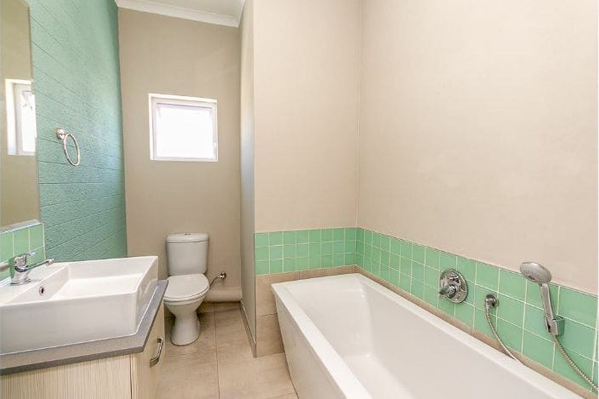 A clean, functional bathroom featuring a modern basin, toilet, and bathtub with green tiled splashbacks and neutral wall finishes.