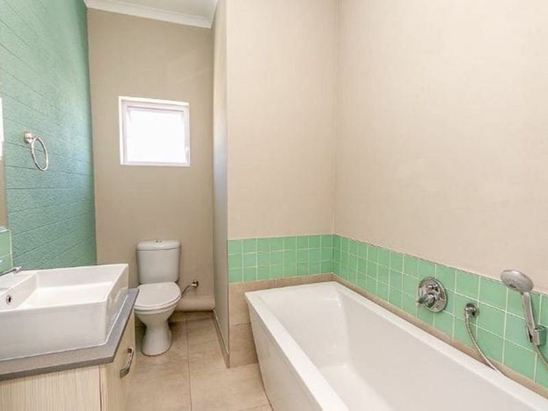 A clean, functional bathroom featuring a modern basin, toilet, and bathtub with green tiled splashbacks and neutral wall finishes.