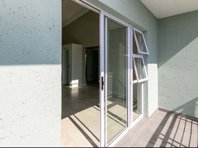 A clean, modern balcony featuring tiled flooring, textured walls, and a large sliding glass door providing access to the interior living space.