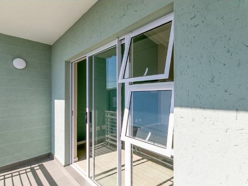 A clean, modern balcony featuring tiled flooring, a sliding glass door, and a top-hung window, providing a bright and functional outdoor space.