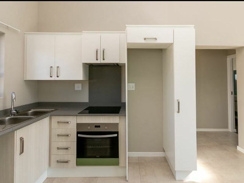 A clean, modern kitchen featuring built-in cabinetry, a stainless steel sink, an electric hob, and an integrated oven with dedicated refrigerator housing.