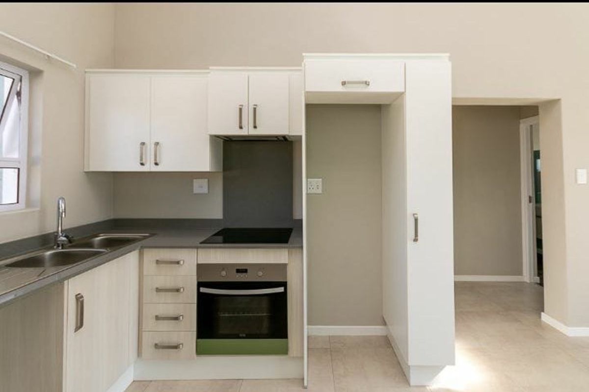 A clean, modern kitchen featuring built-in cabinetry, a stainless steel sink, an electric hob, and an integrated oven with dedicated refrigerator housing.
