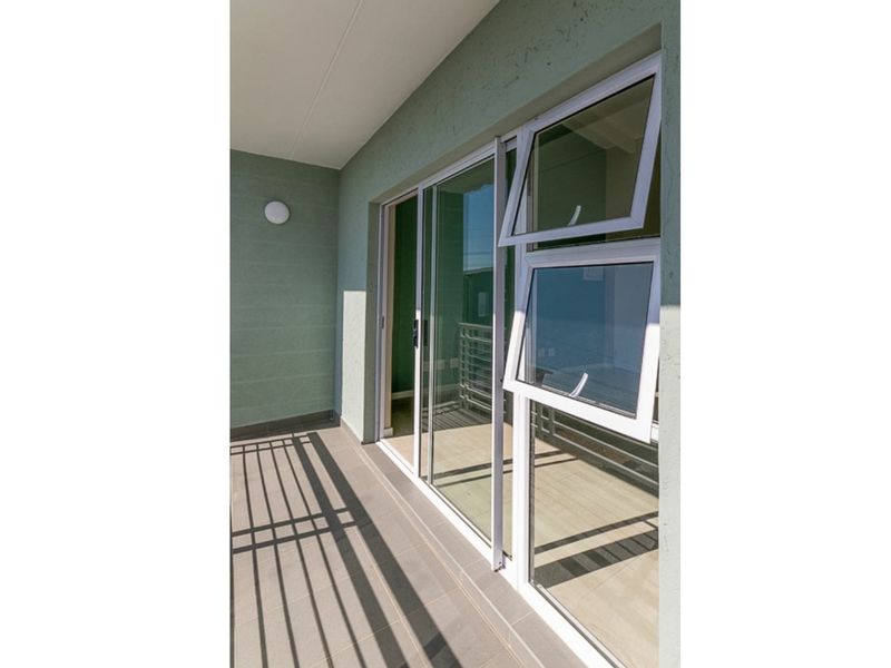A clean, modern balcony featuring tiled flooring, sliding glass doors, and casement windows, providing a bright and functional outdoor space.