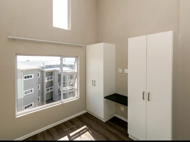 A bright bedroom featuring double-volume ceilings, laminate flooring, built-in cupboards, and a convenient integrated desk area with large windows.