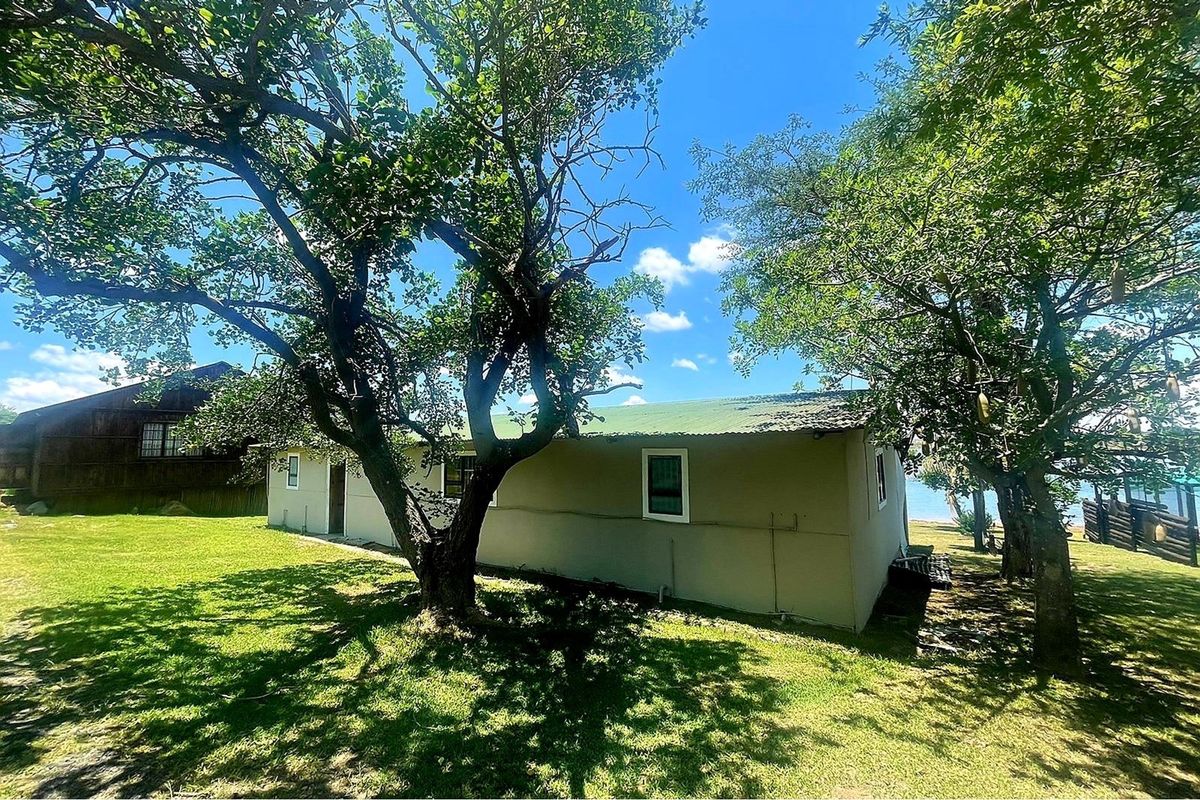A view of the rear exterior of the property, featuring a simple structure set within a spacious, tree-lined garden area.