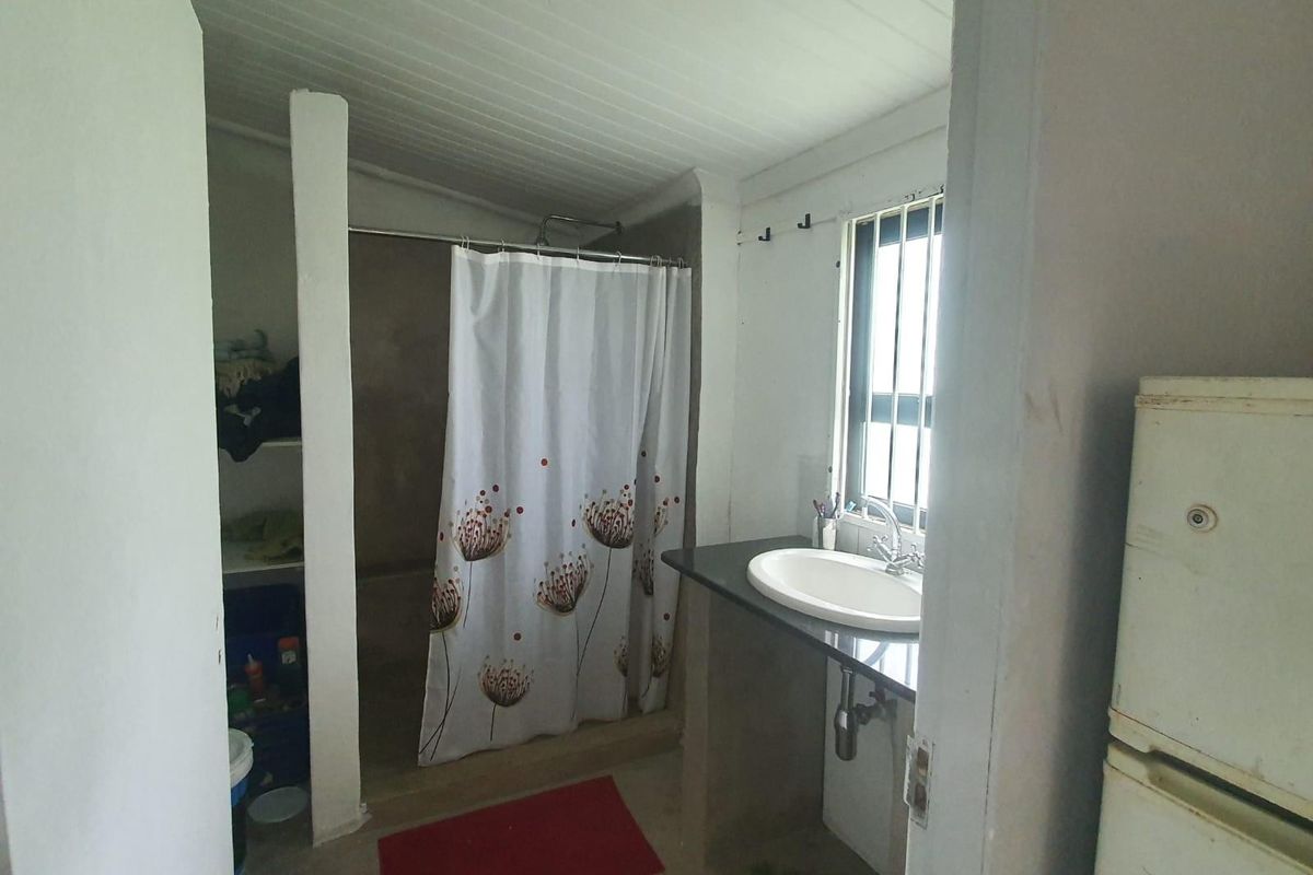 A functional bathroom featuring a shower enclosure, vanity basin with granite countertop, and security bars on the window.