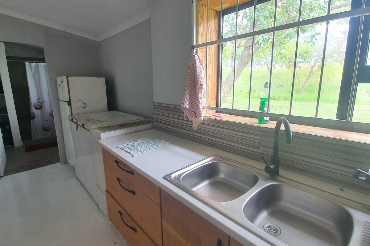 A functional kitchen area featuring a double stainless steel sink, modern matte black faucet, wooden cabinetry, and a window with security bars.