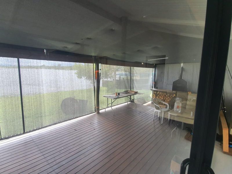 Covered outdoor patio area featuring timber decking, corrugated metal wall cladding, and a built-in fireplace, offering views of the adjacent water.