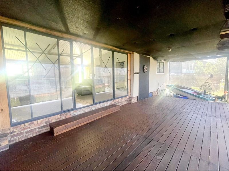 A covered outdoor patio area featuring timber decking, large glass sliding doors, and a brick base, providing a functional space for outdoor living.