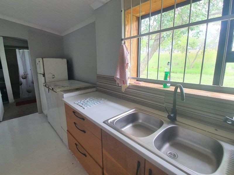 A functional kitchen area featuring a double stainless steel sink, modern matte black faucet, wooden cabinetry, and a window with security bars.