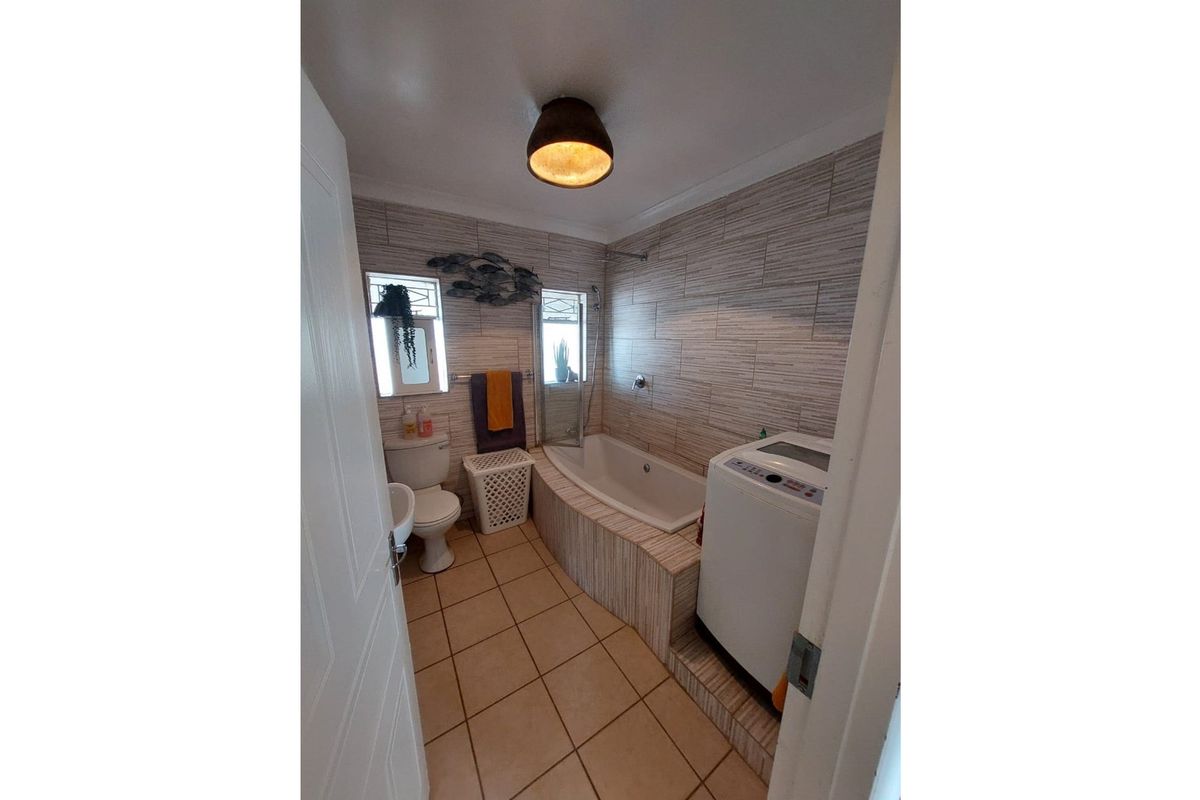 A functional bathroom featuring a built-in bathtub with tiled surround, a toilet, and space for a washing machine.