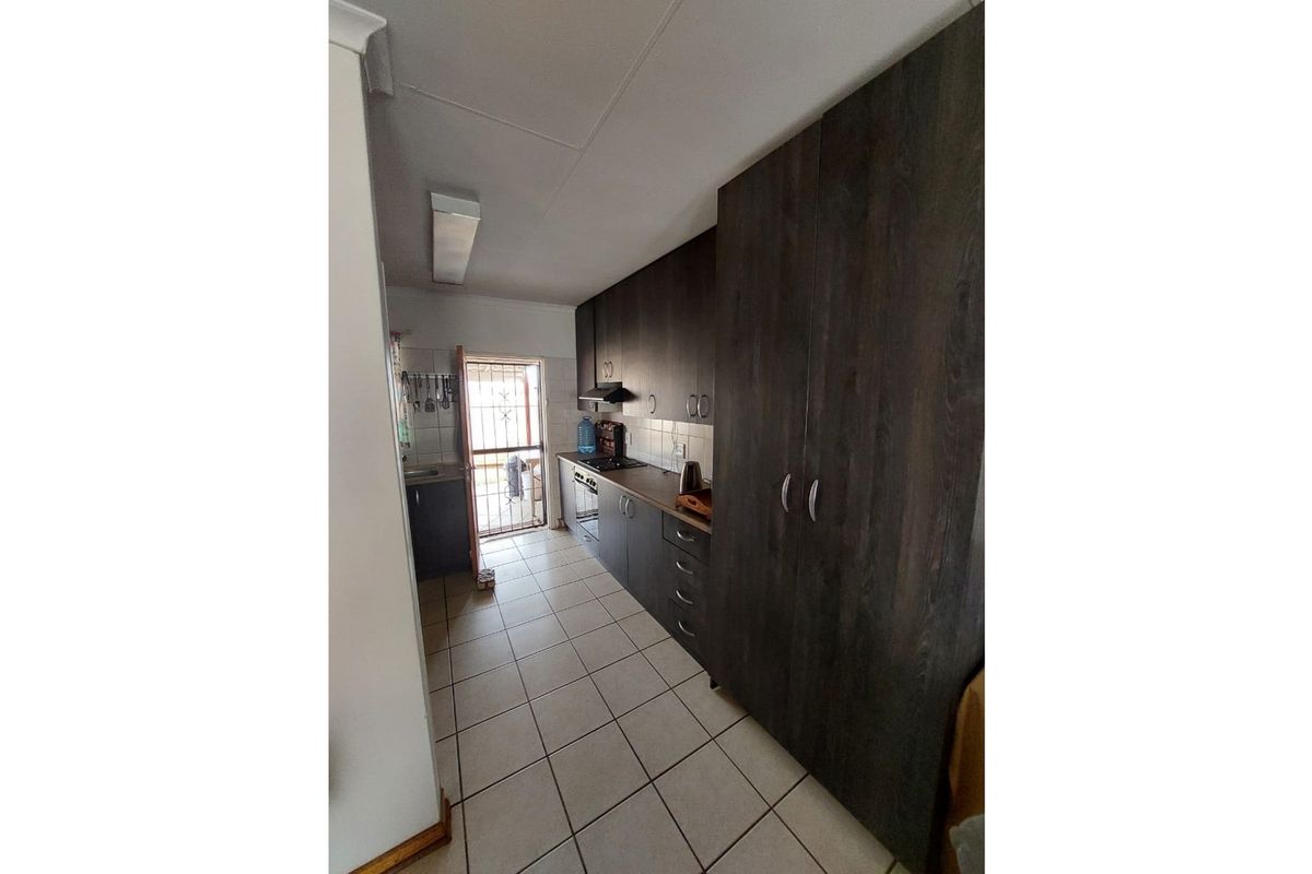 A functional galley-style kitchen featuring dark wood-look cabinetry, built-in oven and hob, and tiled flooring with direct access to an exterior door.