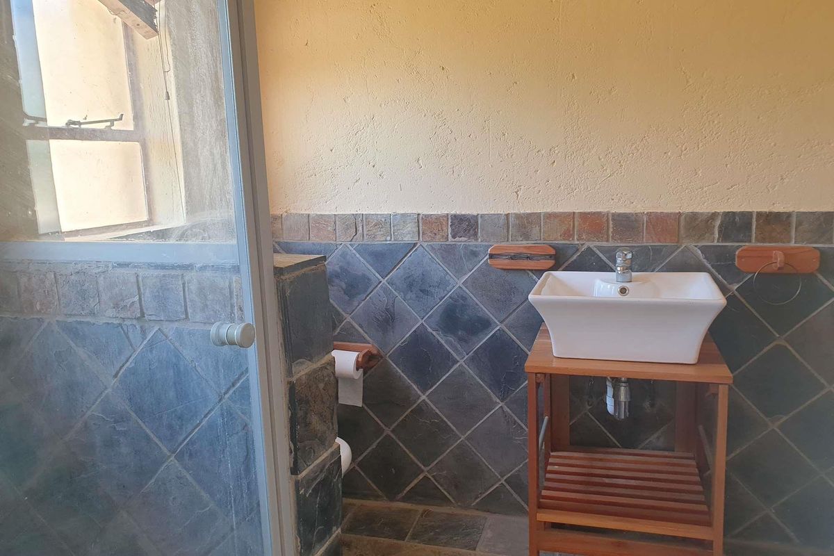 A rustic bathroom featuring slate wall tiling, a vessel sink on a wooden vanity, and a glass shower enclosure.