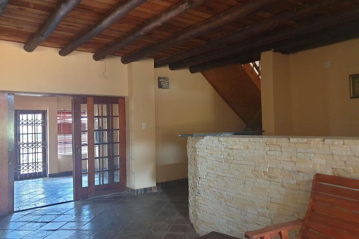 Spacious living area featuring exposed timber beam ceilings, a stone-clad feature wall, and direct access to an adjoining room through French doors.