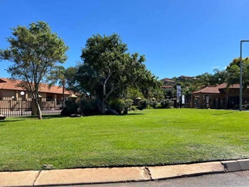 A well-maintained residential vacant land plot featuring lush green lawn, mature trees, and perimeter fencing within a secure estate setting.