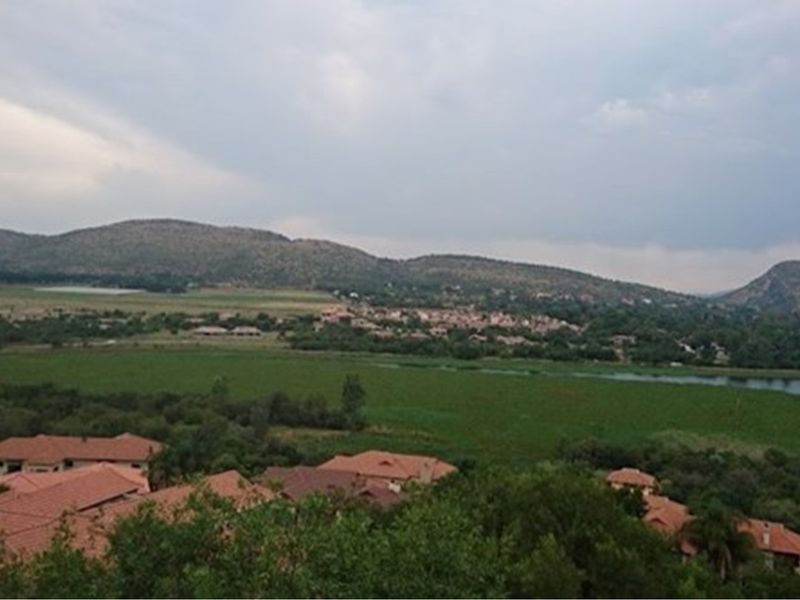 A scenic elevated view overlooking a residential estate, lush green fields, a river, and distant rolling hills.