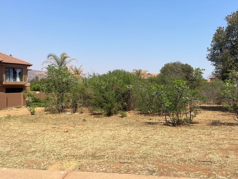 A vacant residential plot featuring natural vegetation and dry grass, situated adjacent to an existing residential property.