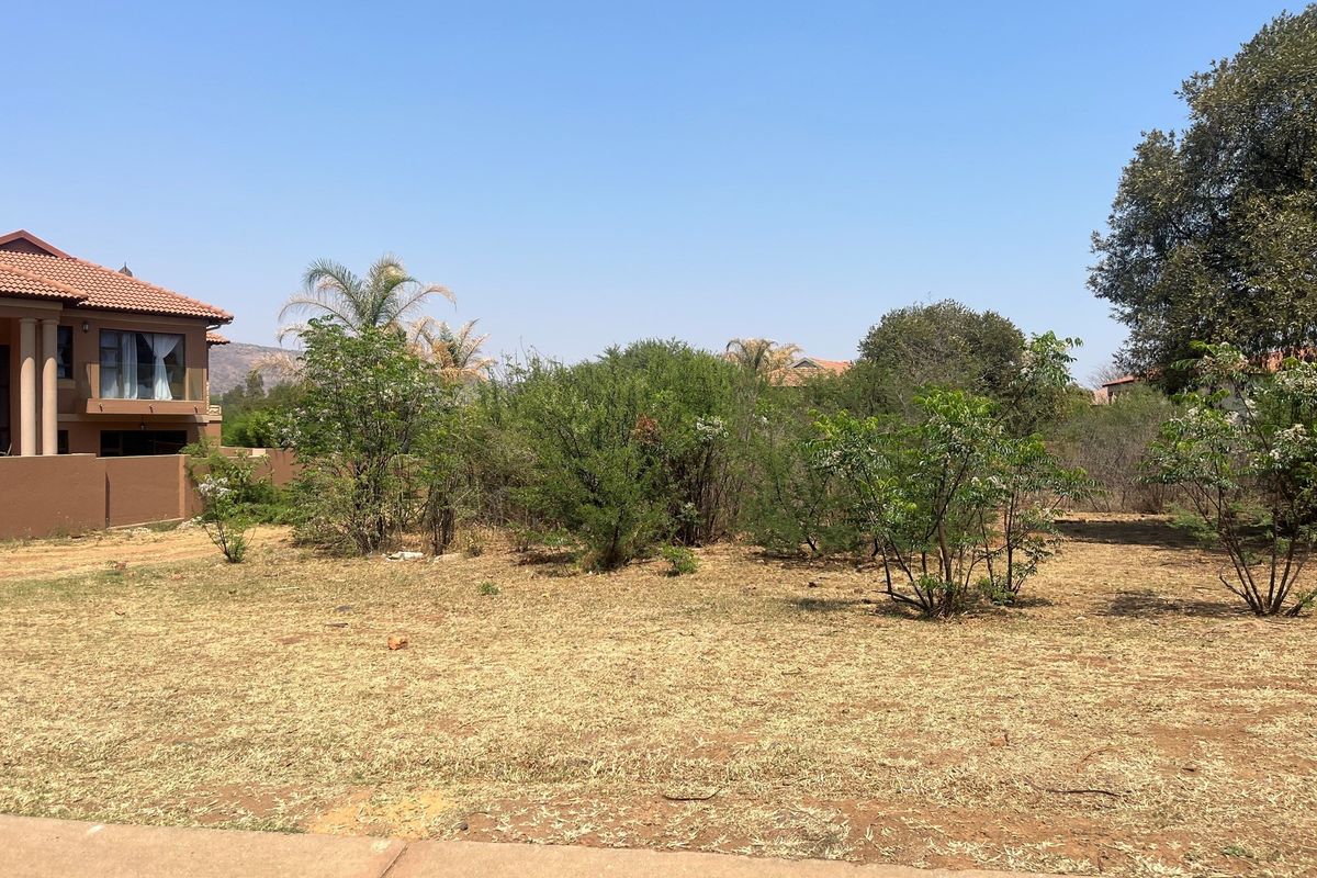 A vacant residential plot featuring natural vegetation and dry grass, situated adjacent to an existing residential property.