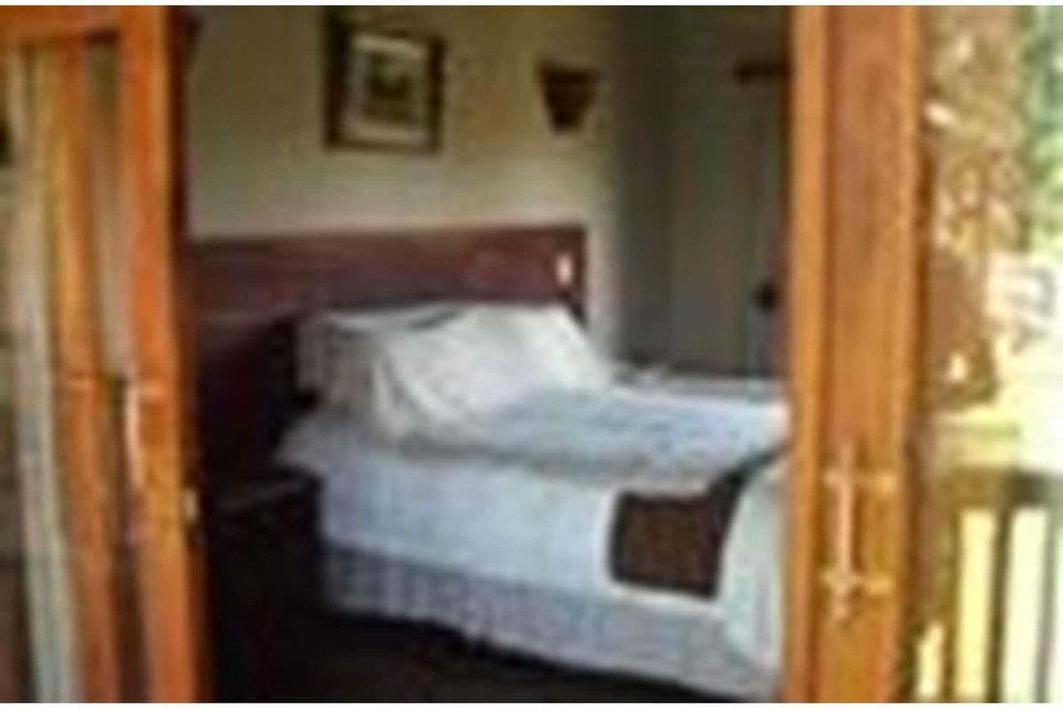 A bedroom featuring a built-in wooden headboard, viewed through wooden framed glass doors.