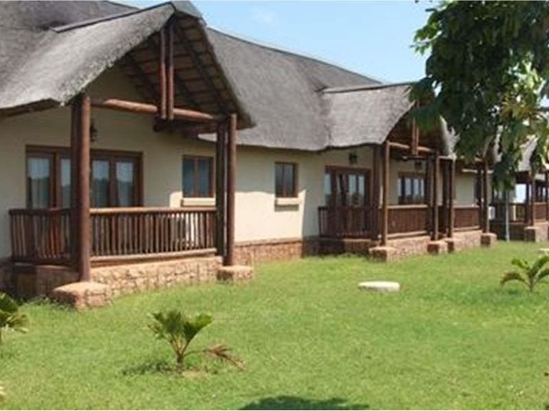 A view of the rear exterior of a farm-style building featuring a thatched roof, timber support beams, and covered patio areas overlooking a lawn.