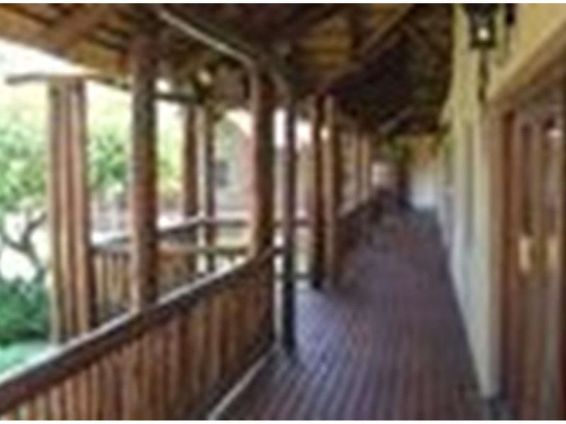 A covered wooden veranda featuring rustic timber support posts and railings, providing a sheltered outdoor walkway along the side of the farm building.