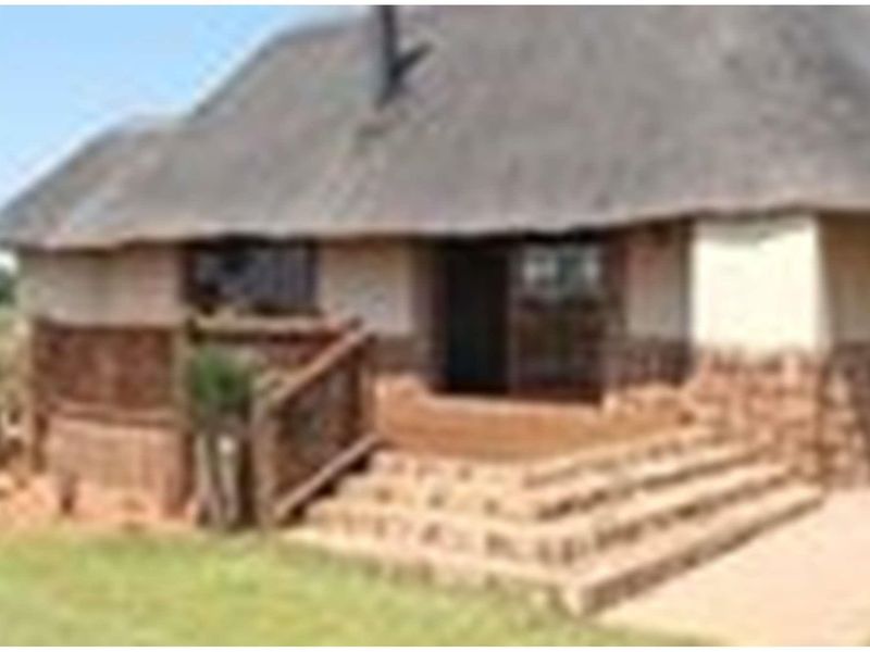 A rustic farm-style dwelling featuring a traditional thatched roof, stone-clad base, and a raised wooden deck entrance with stone steps.