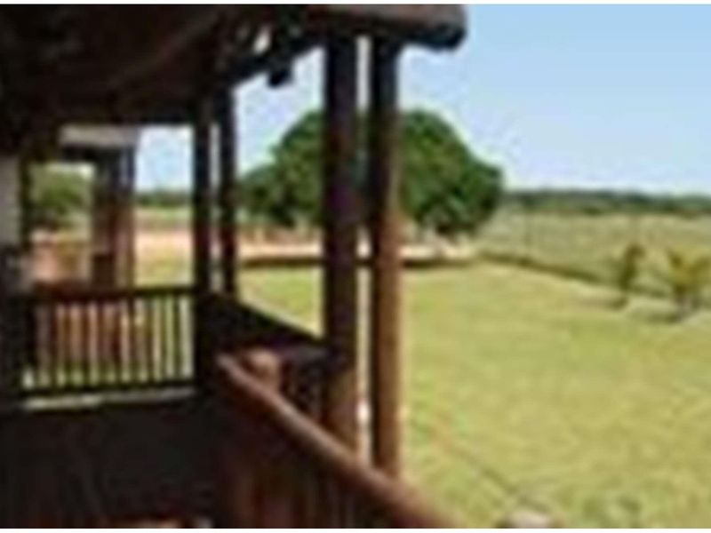 A covered wooden balcony overlooking a spacious farm garden and open landscape.