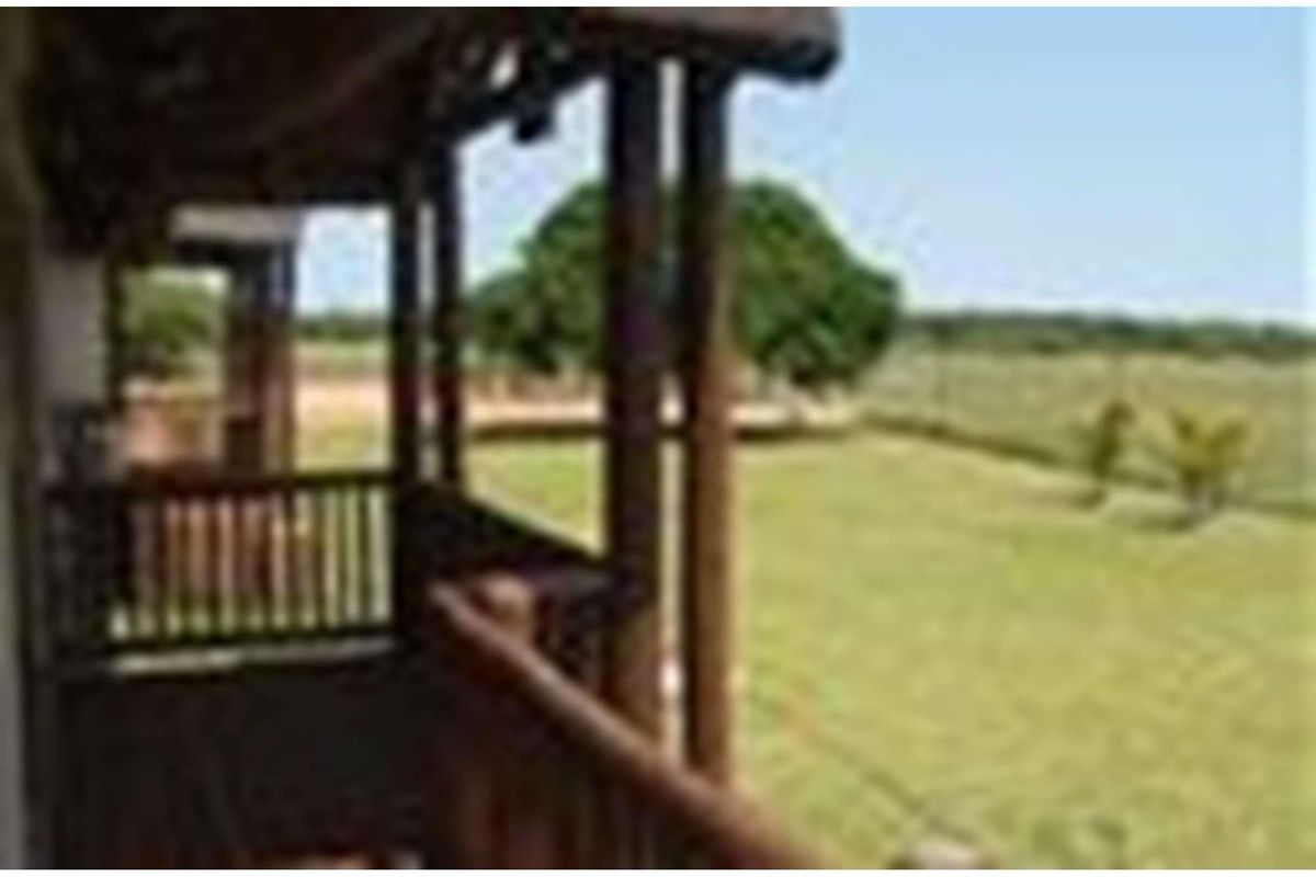 A covered wooden balcony overlooking a spacious farm garden and open landscape.
