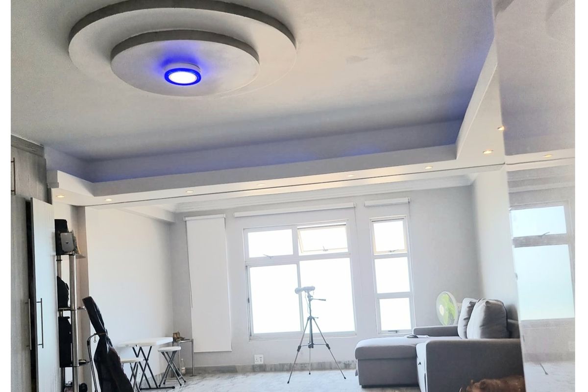 A bright living room featuring a modern recessed tray ceiling with integrated LED accent lighting and large windows providing ample natural light.