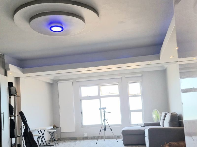 A bright living room featuring a modern recessed tray ceiling with integrated LED accent lighting and large windows providing ample natural light.