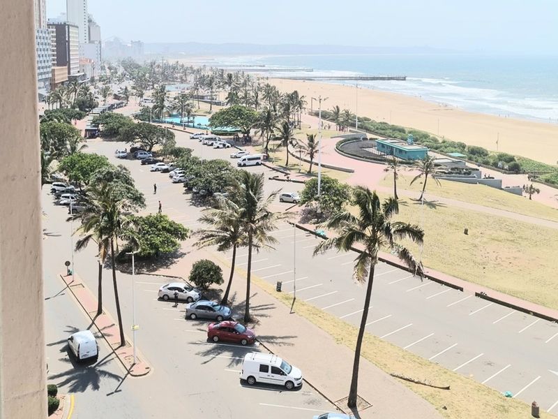Elevated view overlooking the coastal promenade, public parking area, and sandy beach.