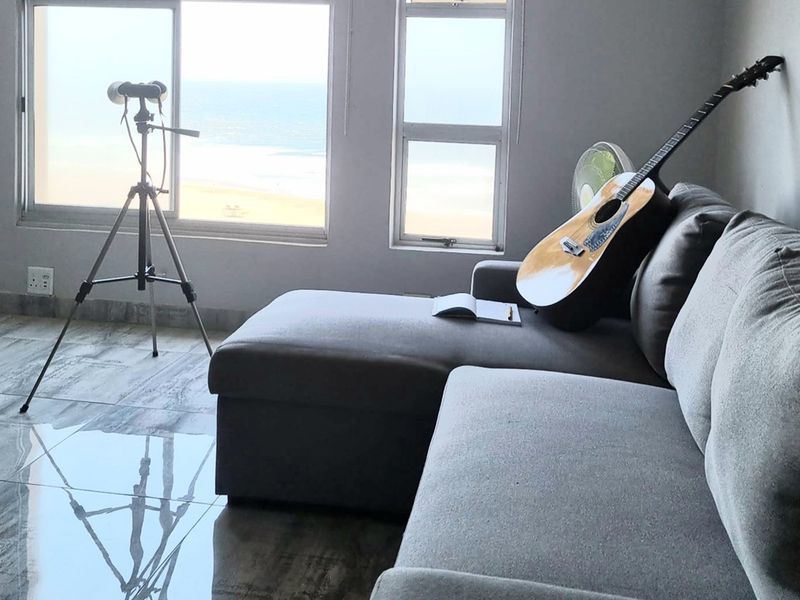 A bright living room featuring large windows with ocean views, polished tiled flooring, and a neutral interior finish.