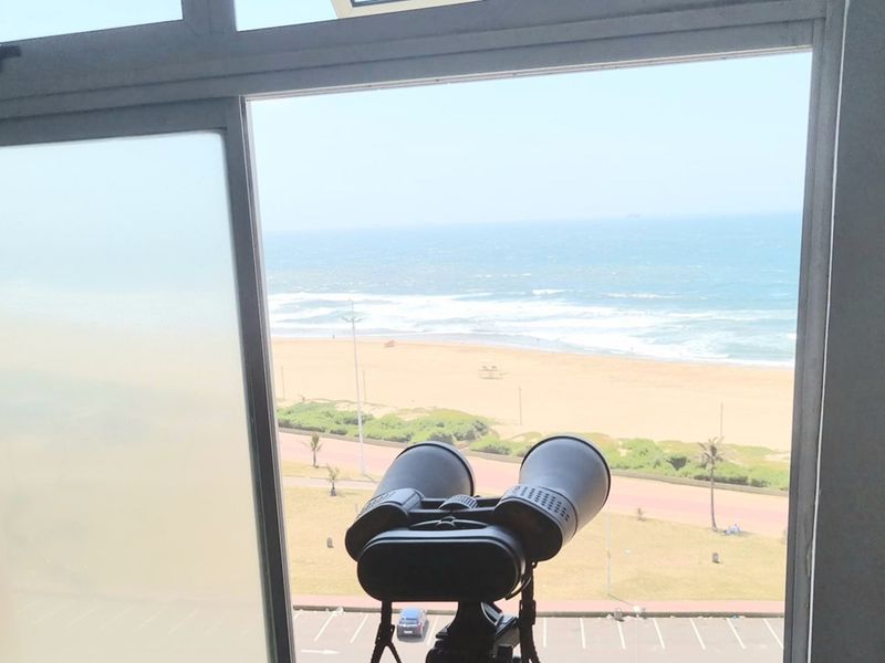 A view of the beach and ocean from an interior window, featuring a clear outlook over the coastal promenade.