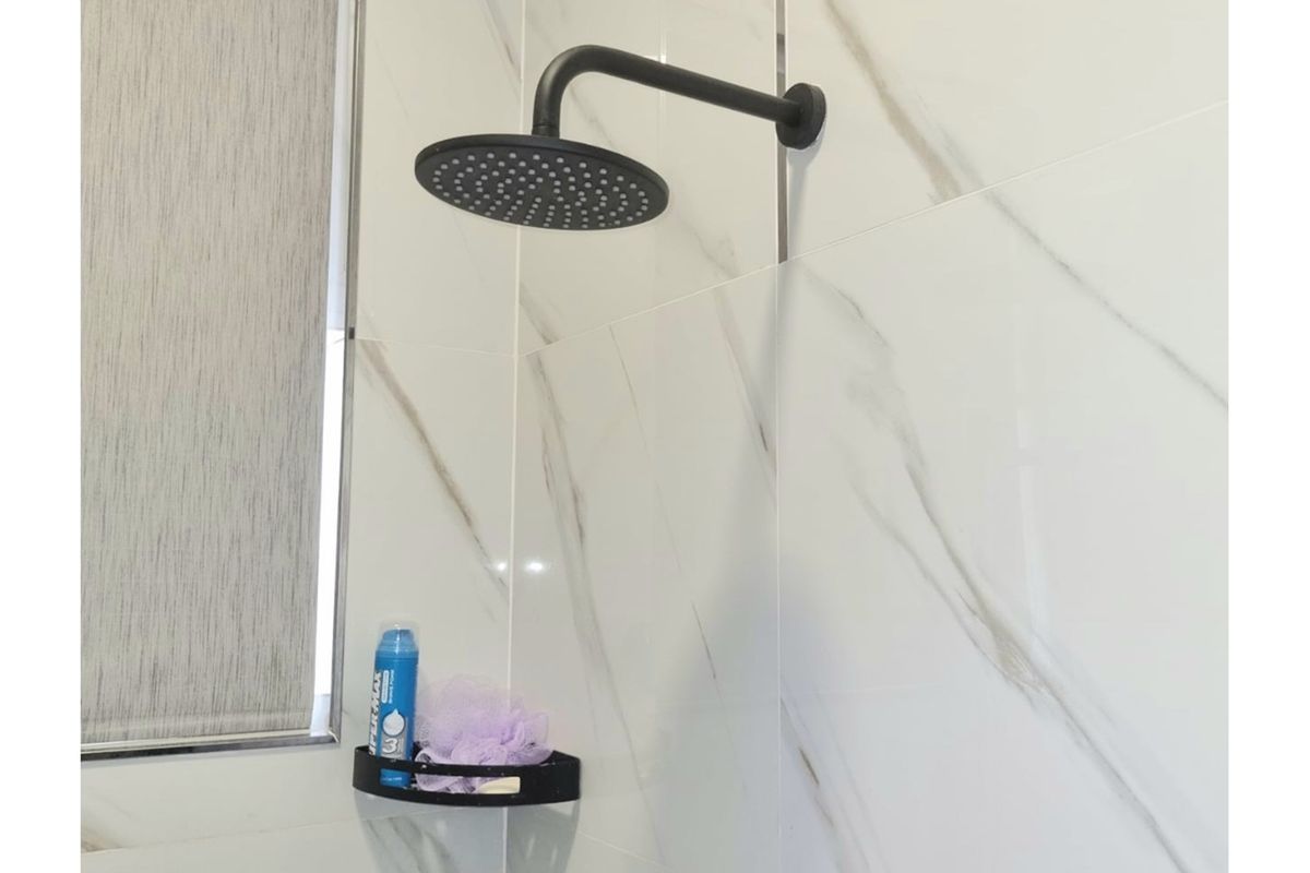 Modern bathroom shower area featuring large-format marble-look wall tiles and a contemporary matte black rainfall shower head.