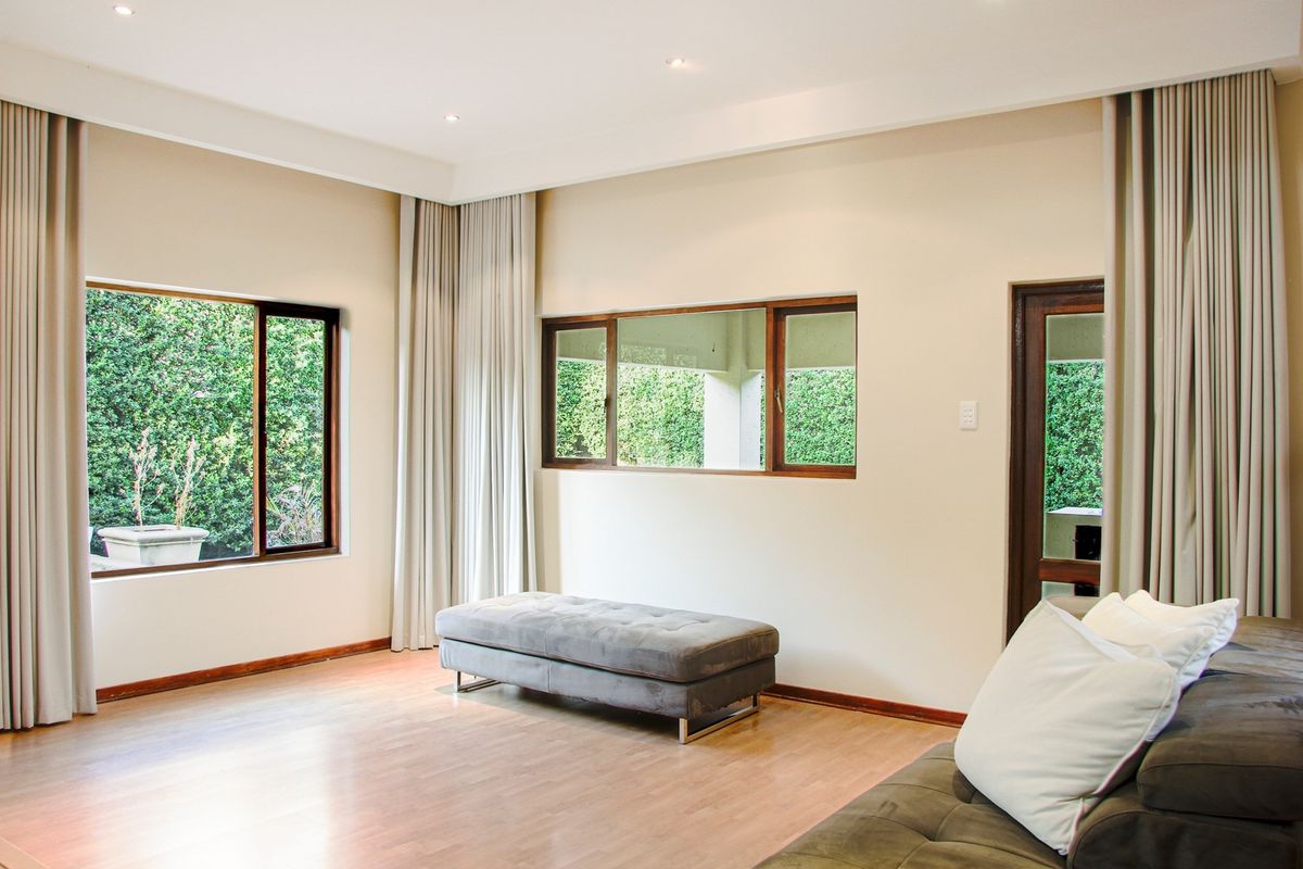A bright living room featuring laminate flooring, recessed downlights, and large windows with timber frames, offering a view of the garden.