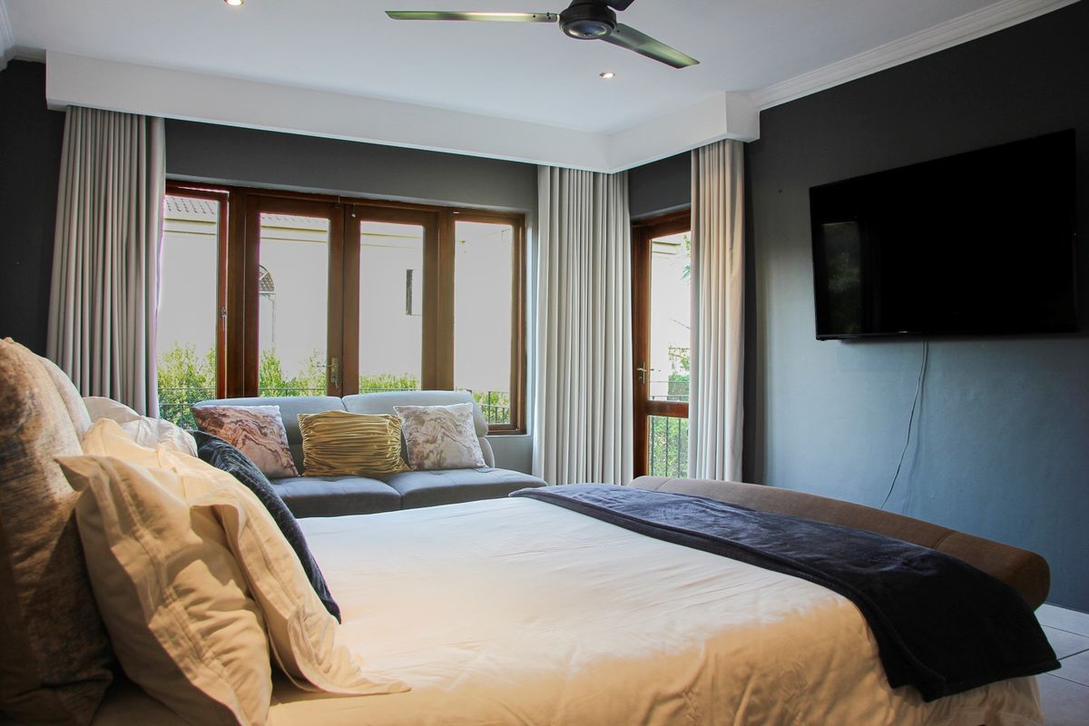 A well-maintained bedroom featuring dark accent walls, crown molding, recessed lighting, a ceiling fan, and timber-framed doors leading to an outdoor area.