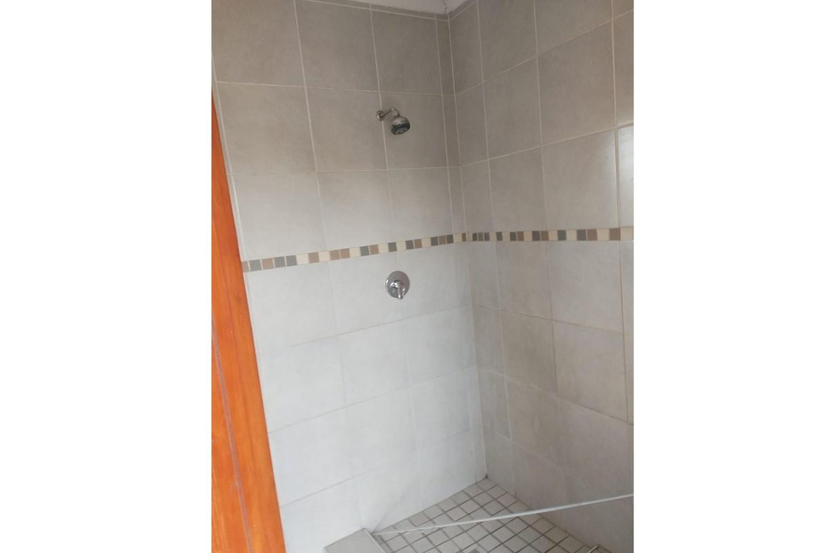 A functional shower enclosure featuring neutral wall and floor tiling with a standard shower head and mixer tap.