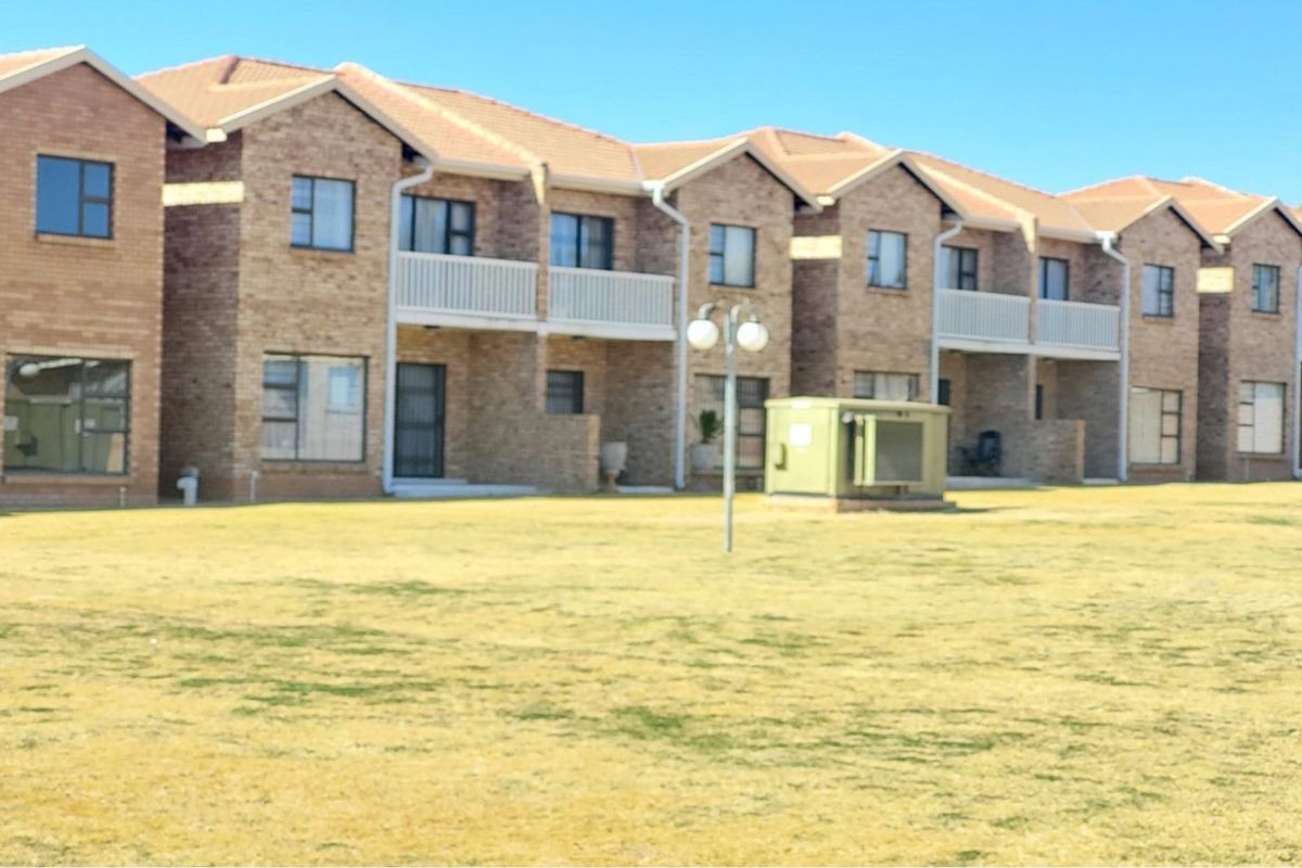 A view of the rear facade of a multi-unit residential complex featuring face-brick construction, tiled roofs, and upper-level balconies overlooking a communal lawn area.