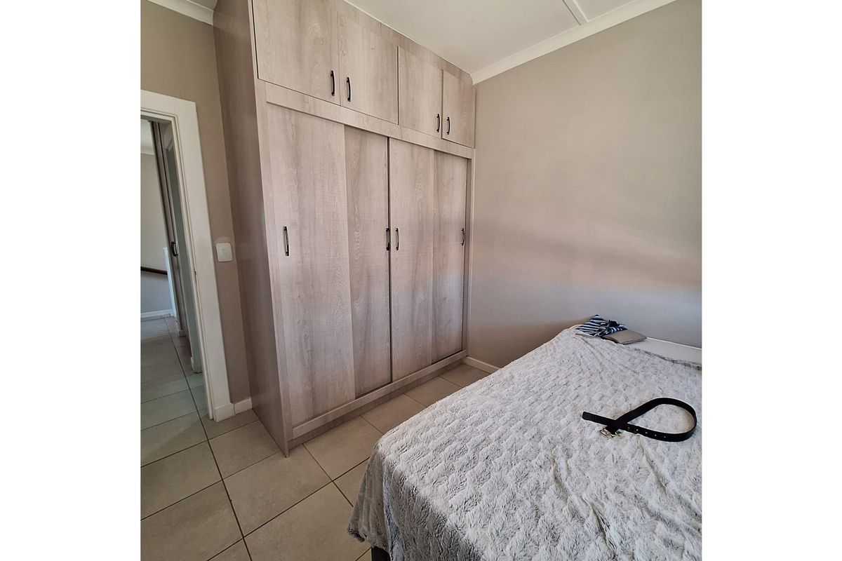 A well-maintained bedroom featuring light wood-grain built-in cupboards with overhead storage and neutral tiled flooring.