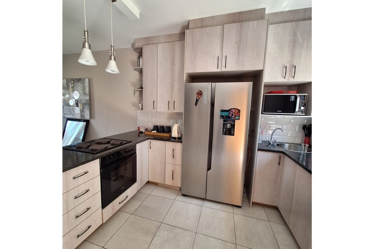 Modern kitchen featuring light wood-grain cabinetry, dark granite countertops, subway tile backsplash, and integrated oven with electric hob.