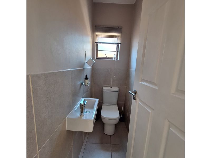 A compact guest bathroom featuring a wall-mounted basin, modern toilet, and neutral tiled finishes.