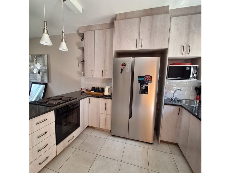Modern kitchen featuring light wood-grain cabinetry, dark granite countertops, subway tile backsplash, and integrated oven with electric hob.