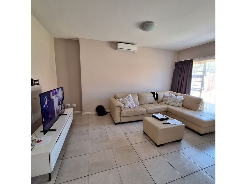 A living room featuring tiled flooring, a wall-mounted air conditioning unit, and sliding glass doors leading to an outdoor area.