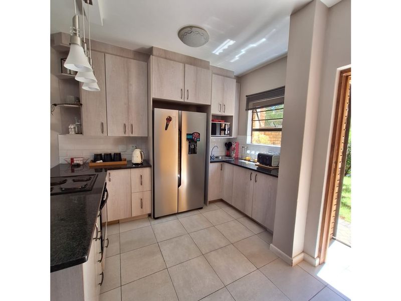 Modern kitchen featuring light wood cabinetry, dark granite countertops, tiled flooring, and direct access to the outdoor area.