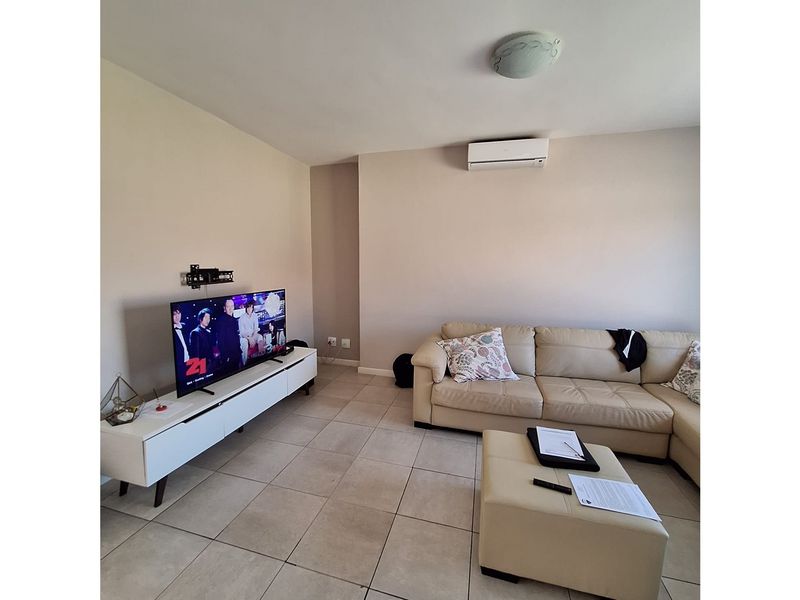 A living room featuring tiled flooring, a wall-mounted air conditioning unit, and a ceiling light fixture.