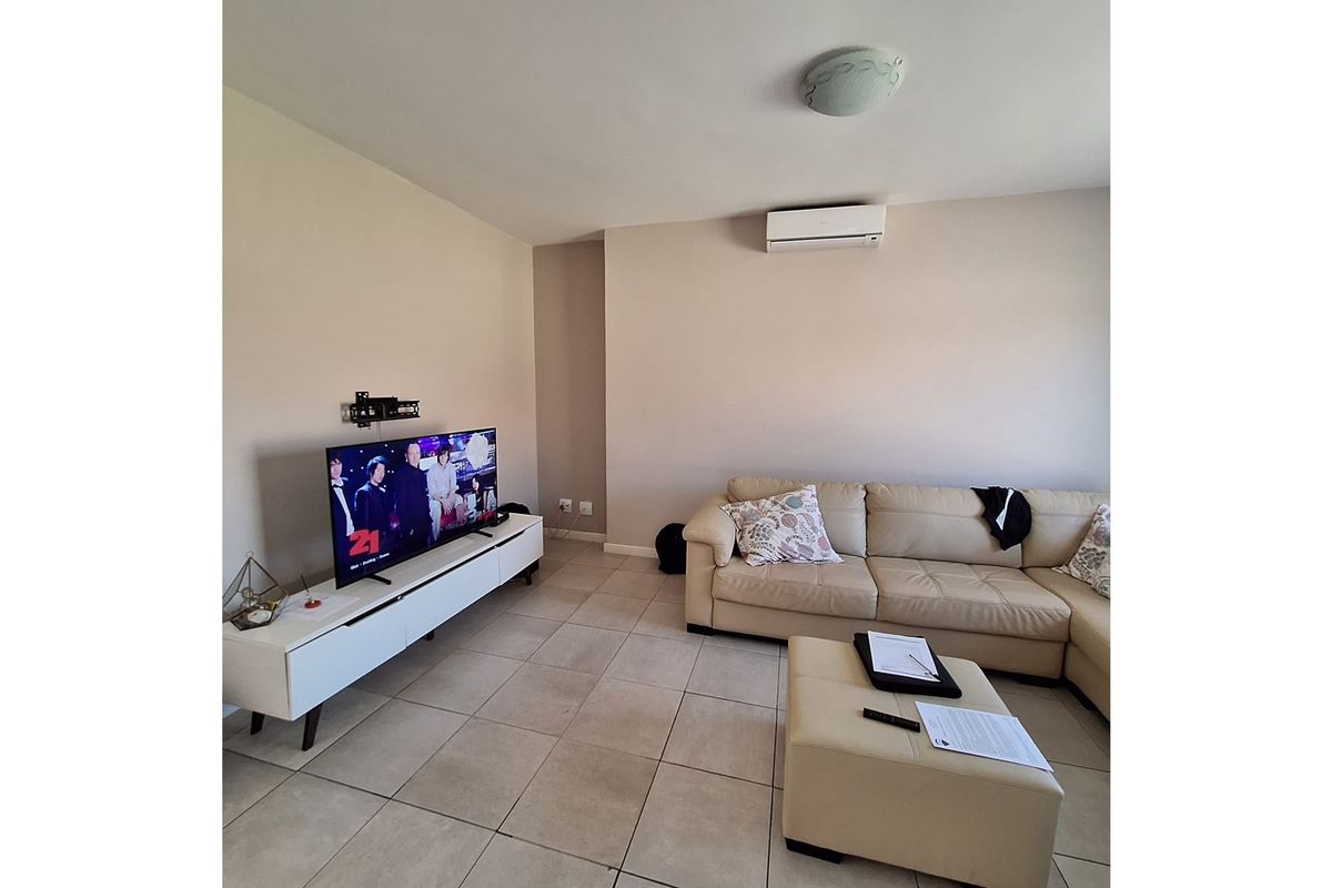 A living room featuring tiled flooring, a wall-mounted air conditioning unit, and a ceiling light fixture.